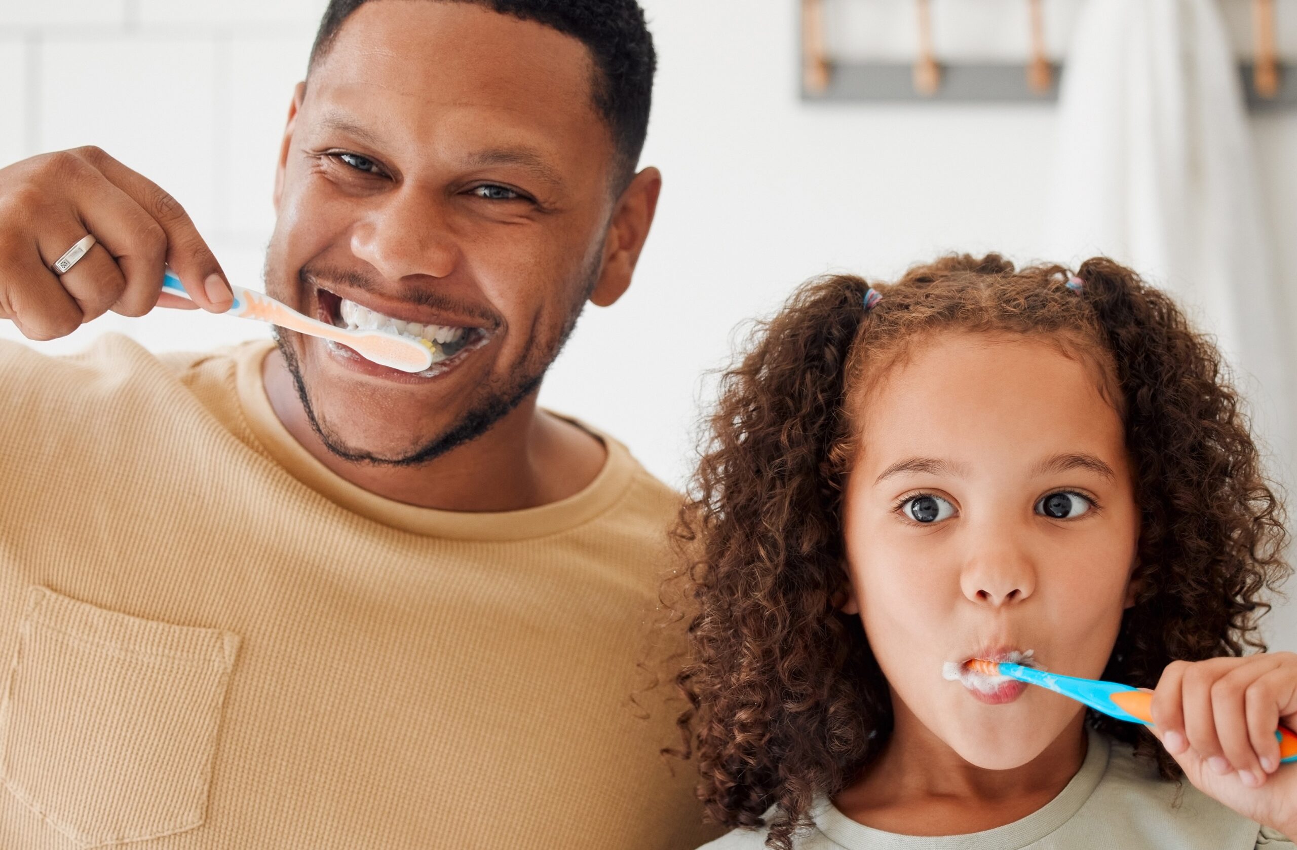 smiling duo of father and daughter brushing their teeth