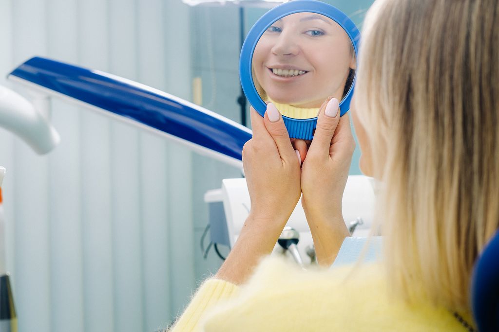 a girl smiling looking at dental mirror